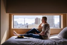 Man relaxes on a bed, gazing at a city view.