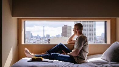 Man relaxes on a bed, gazing at a city view.