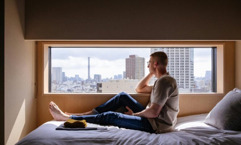 Man relaxes on a bed, gazing at a city view.