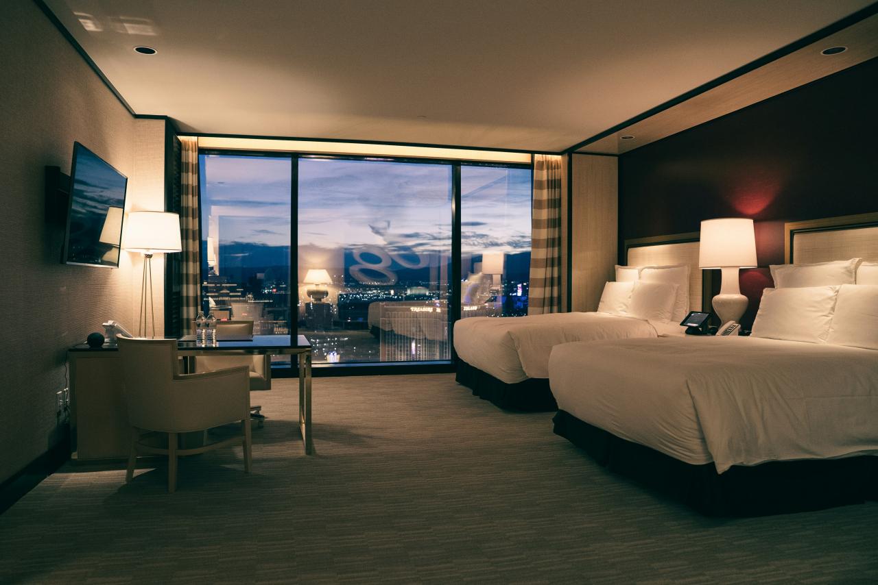 Luxurious hotel room with two beds and city view.